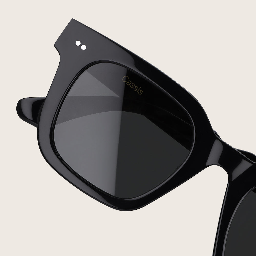 Black sunglasses with 'Cassis' branding on a beige background